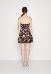 Svart bandeauklänning med blommönster; lager av volanger vid fållen; tyget verkar slätt. Kombinerad med gröna snörboots.