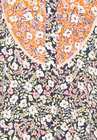 Blusa com padrão floral em tecido laranja e azul-marinho. Os detalhes incluem botões pretos e um colarinho contrastante com acabamento em rosa claro.