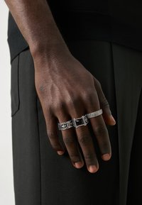 Silver rings on a dark-skinned hand; one features a rectangular black stone, another has intricate patterns, and a third is twisted.