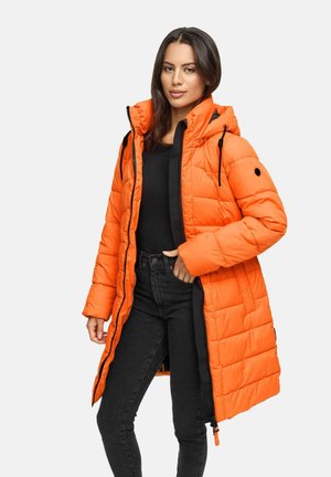 Woman wearing bright orange quilted winter coat with hood, black top, and black jeans, standing against plain white background.