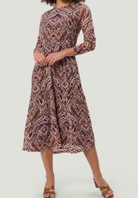 Robe longue en tissu multicolore à motifs avec des nuances de bordeaux, crème et marron. Manches longues et jupe à volants.
