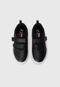 Baskets Puma noires et rouges avec des двойные sangles Velcro et des semelles blanches, vues de dessus sur un fond blanc.