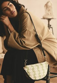 Piccola borsa a spalla con una forma curvata; motivo floreale in verde e bianco; tracolla e dettagli neri; materiale in tessuto con una texture liscia.