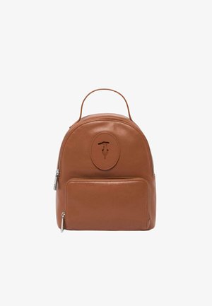 Sac à dos en cuir marron avec une forme arrondie, poche zippée à l'avant et accent logo circulaire. Il dispose d'une poignée supérieure pour le transport.