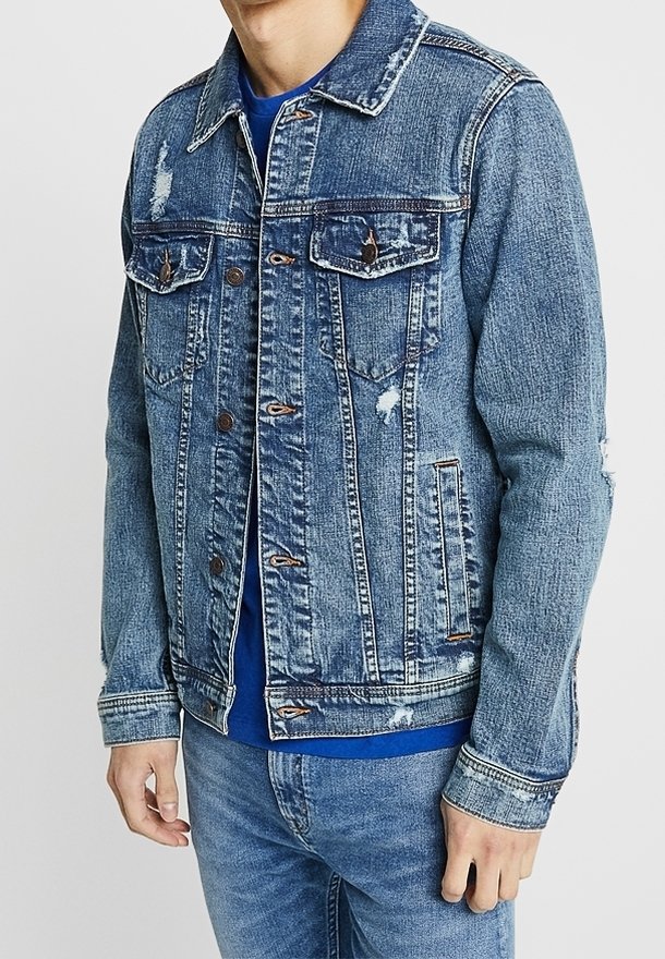 Denim jacket in light blue with a distressed design, featuring two chest pockets, metal buttons, and buttoned cuffs. Worn over a blue shirt.