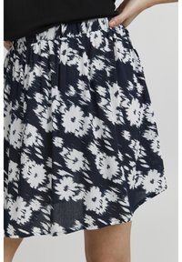 Blomstret nederdel lavet af plisseret stof, med et mønster i navy og hvid med abstrakte blomster. Elastisk talje, knælang model.