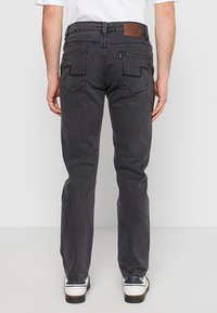 Szare dżinsy o wąskim kroju, z skórzaną naszywką z logo z tyłu, zakrzywionymi tylnymi kieszeniami i subtelnymi detalami szwów.