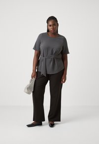 Gray short-sleeve top with a tied waist detail, paired with black wide-leg trousers and black flat shoes. The person carries a silver patterned bag.