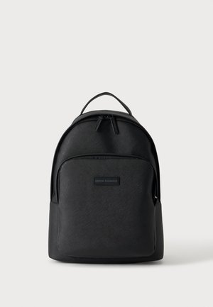 Sac à dos noir Armani Exchange avec poche zippée à l'avant, poignée supérieure et matière texturée sur un fond clair uni.