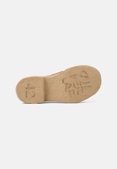 Zool van een schoen in lichtbeige, gestructureerd rubber met een robuust ontwerp. Bevat verhoogde letters en geometrische patronen aan de onderkant.