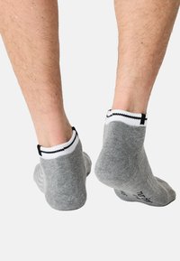 Szare skarpetki do kostek z prążkowanym białym mankietem i czarnymi akcentami, charakteryzujące się gładką fakturą oraz logo nadrukowanym na podeszwie.