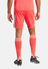 Hellorange Sportanzug mit einem kurzärmeligen Shirt und passender Shorts. Enthält kniehohe Socken mit weißen Akzenten und schwarze Fußballschuhe.