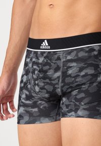 Moške športne bokserice v črno-sivi kamuflažni vzorcu, z črnim elastičnim pasom, na katerem je bel Adidasov logotip in kontrastno šivanje.