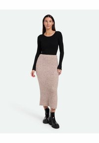 Top negru cu dungi, cu mânecă lungă, asortat cu o fustă midi tricotată texturată de culoare roz deschis, completat de botine negre lucioase cu talpă groasă.