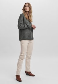 Pull en tricot vert foncé à manches longues, pantalon beige moulant et bottes à talons marron avec un motif crocodile. Silhouette simple et décontractée.