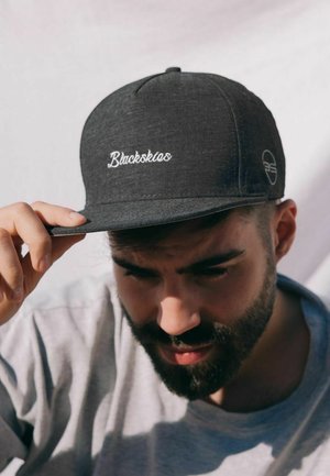 Sivi kapu od teksturiranog materijala sa bijelim izvezenim tekstom "Blackskies." Šilt je ravan, a logo detalj se pojavljuje sa strane.