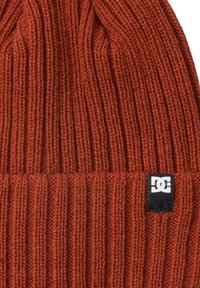 Gorro de punto de color óxido, con textura acanalada y un dobladillo. Presenta una pequeña etiqueta negra con un logo blanco en el lado.