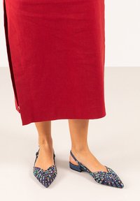 Bailarinas de punta afilada y con tira en el talón, adornadas con cuentas multicolores, de tela azul y con un bajo tacón kitten, combinadas con una falda roja.