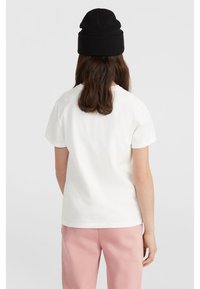 Vit bomull t-shirt med korta ärmar och rund halsringning, tillsammans med ljusrosa byxor. En svart stickad mössa fulländar outfiten.