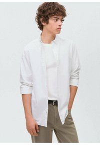 Camicia bianca a bottoni sopra una t-shirt bianca, abbinata a pantaloni beige. Presenta maniche lunghe, vestibilità casual e colletto.