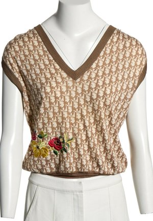Haut en maille sans manches beige et marron avec col en V, motif monogramme, et fleurs rouges et jaunes brodées sur le côté.