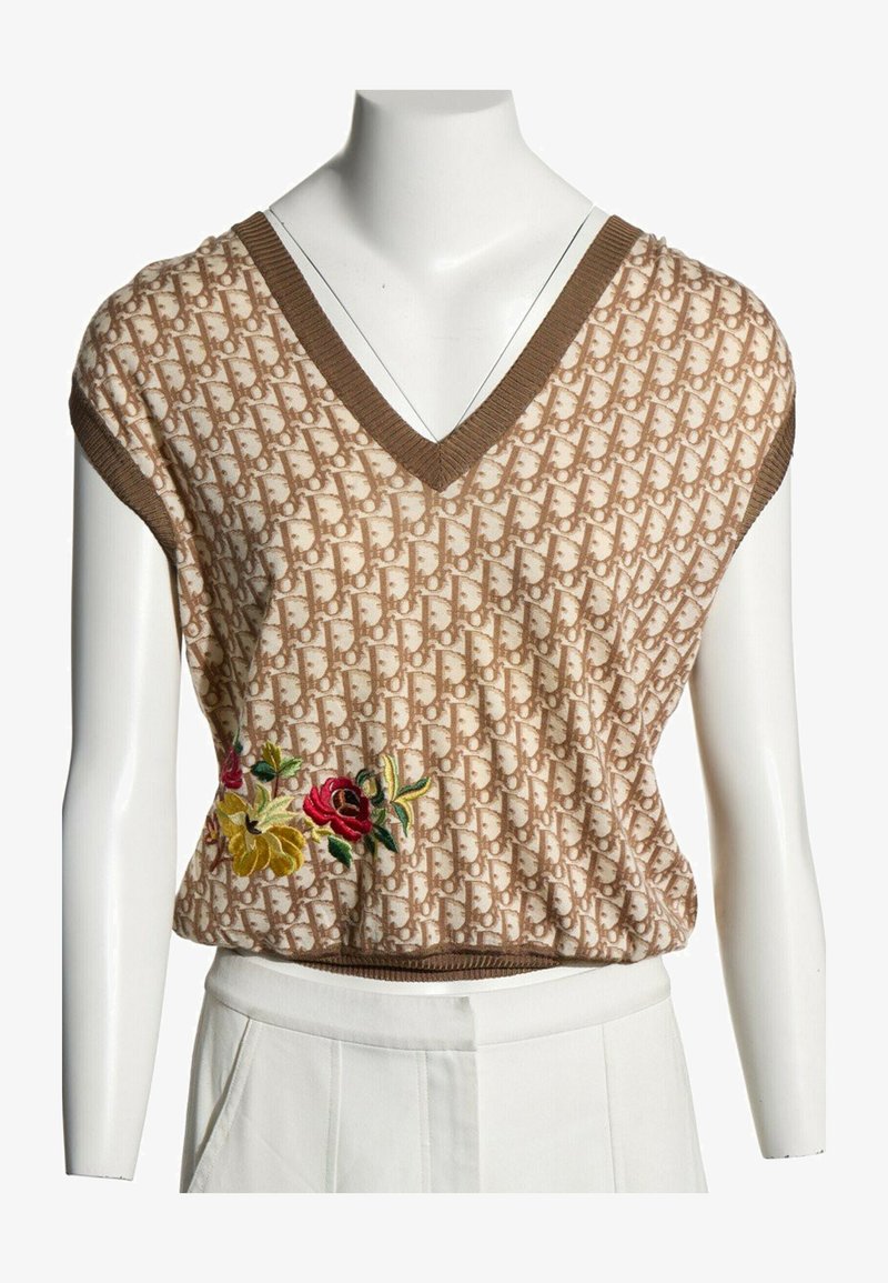 Haut en maille sans manches beige et marron avec col en V, motif monogramme, et fleurs rouges et jaunes brodées sur le côté.