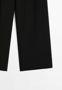 Pantalon noir à jambes larges et droites étalé à plat sur une surface blanche, montrant la partie inférieure des deux jambes.