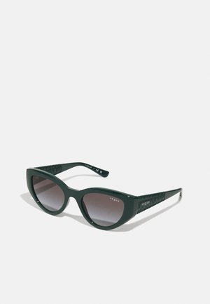 Gafas de sol de plástico verde con forma de ojo de gato, lentes de gradiente oscuro y brazos laterales con patrón texturizado. Marca en la patilla.