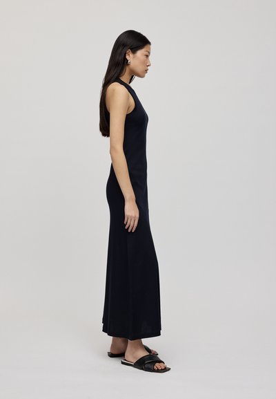 Abito lungo senza maniche di colore navy con corpetto aderente e gonna fluida, abbinato a sandali neri piatti. Tessuto morbido e design minimalista.