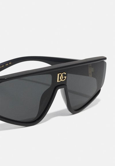 Occhiali da sole neri e angolari con lenti scure. Presentano un logo DG dorato sul frontale, finitura opaca e aste spesse. Design audace e moderno.
