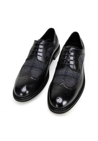 Zwarte leren schoenen met een bovenwerk van wol en een blauw ruitpatroon, afgeronde neus en decoratieve perforaties langs de randen.