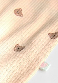 Soft, ribbed fabric in pastel peach with brown bear patterns. Features a multi-colored tag with a heart accent.