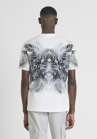 Camiseta de algodón blanca con un gráfico detallado de una hoja de palma en negro y azul en la parte posterior, mangas cortas y un cuello redondo clásico.