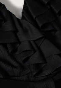 Tissu noir texturé avec des plis superposés et froncés créant un motif doux et fluide sur un fond clair.