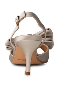 Korkokenkä, jossa on vaaleanbeige satiinipäällinen, pyöreä varvas, nilkkahihna kultaisella soljella ja koristeellinen kaari kantapäässä.