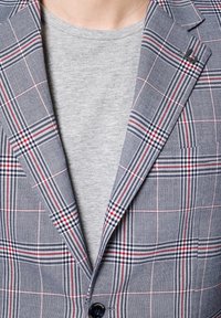 Szary marynarka w kratę z niebieskimi, czerwonymi i białymi akcentami, z wyłamiem, dwoma guzikami i kieszonką na piersi, noszona na szarym koszuli.
