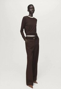 Bluză maro cu mânecă lungă și guler alb, asortată cu pantaloni maro cu talie înaltă. Textură netedă, croială ajustată și pantofi maro cu vârf ascuțit.