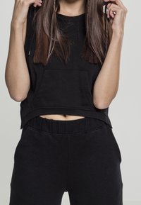 Zwarte korte tanktop met een voorkoffer en ronde halslijn, gecombineerd met bijpassende zwarte hoge taille broeken. Zachte stof en een ontspannen pasvorm.
