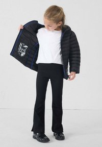 Giacca trapuntata nera con dettagli blu, design trapuntato e motivo grafico interno. Abbinata a una maglietta bianca e pantaloni neri a zampa.