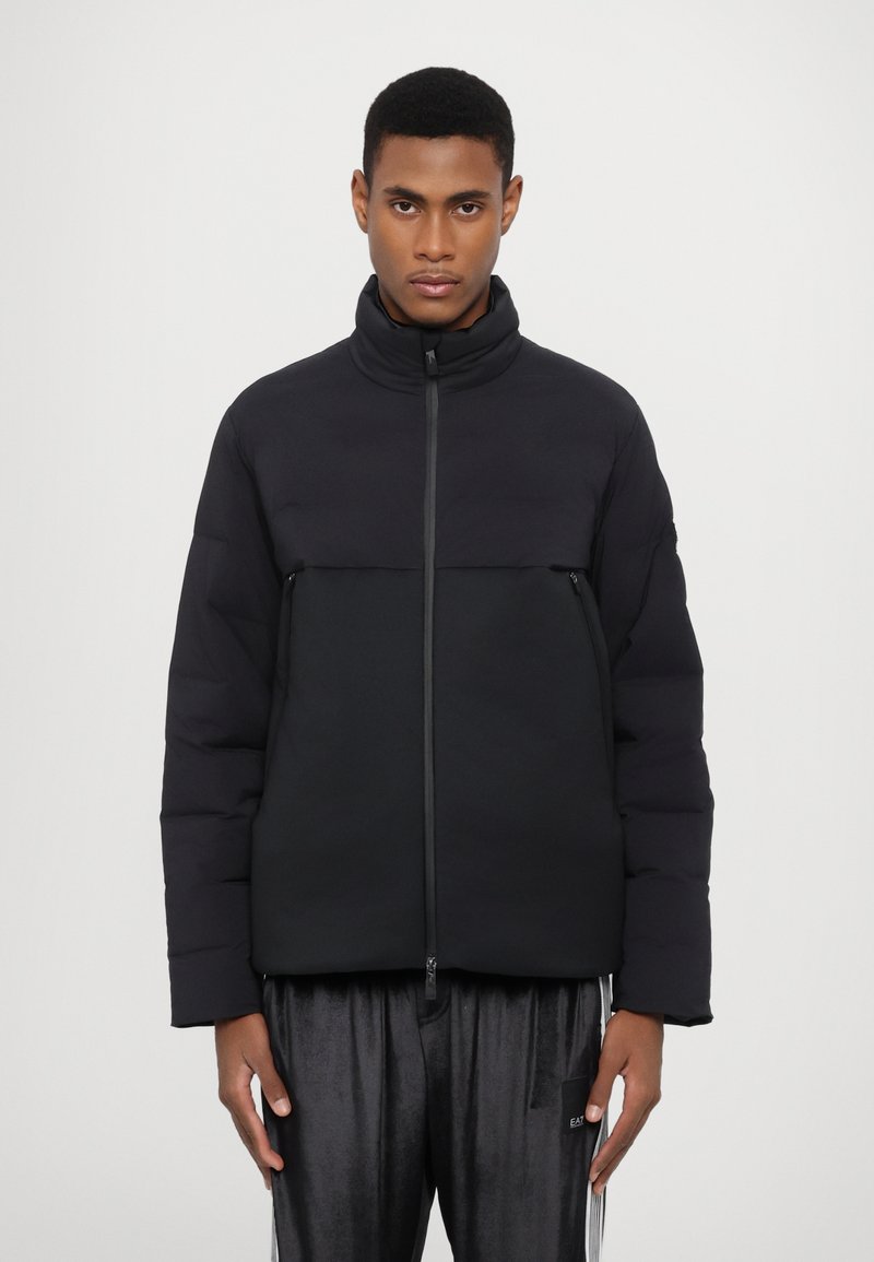 Puffer jacket in black, with a high collar and a zip closure. Features a two-tone design with a smooth upper and textured lower section.