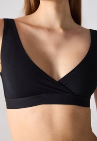 Bralette nera senza cuciture con scollo a V profondo, design avvolgente e spalline larghe. Tessuto morbido e elasticizzato con delicati dettagli di arricciatura al centro.