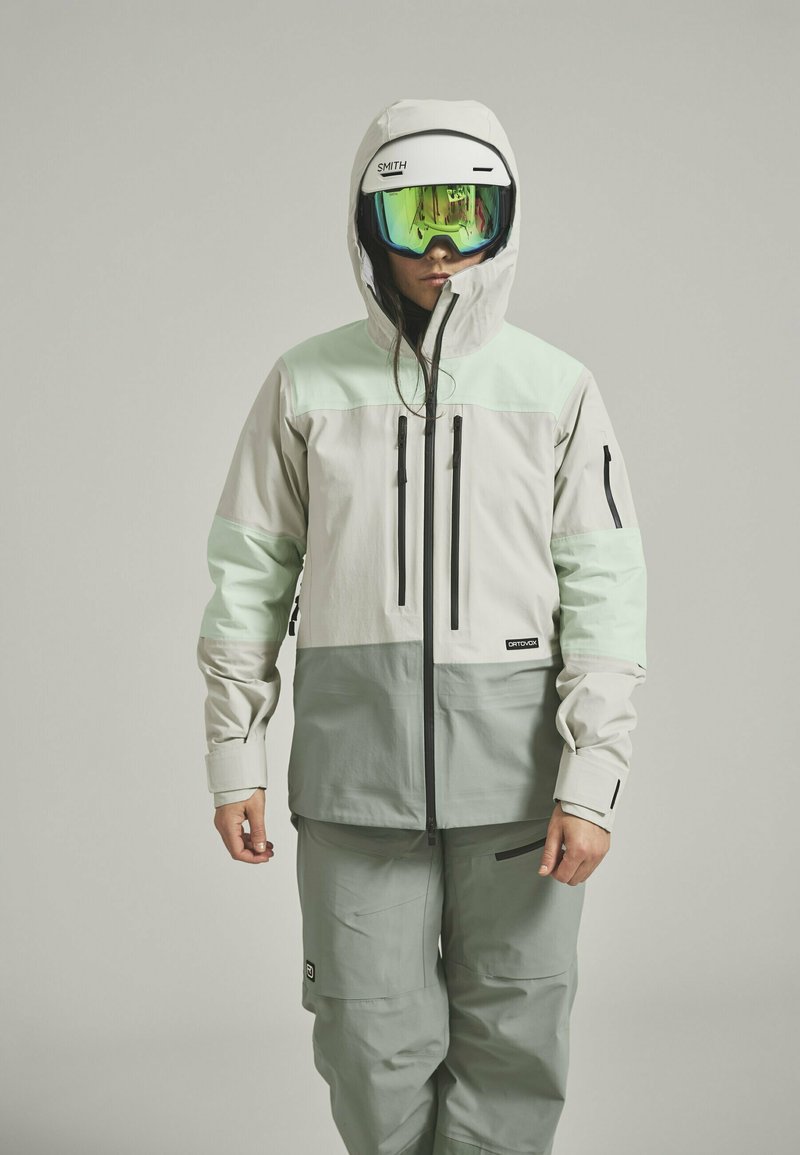 Ski jacket with a light gray and mint green color scheme, featuring a zippered front, multiple pockets, and a helmet-compatible hood.