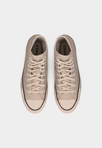 Ζεύγος μπεζ χαμηλών πάνινα παπούτσια με λευκά κορδόνια και λεπτομέρεια μαύρης ρίγας, από πάνω, σε λευκό φόντο.