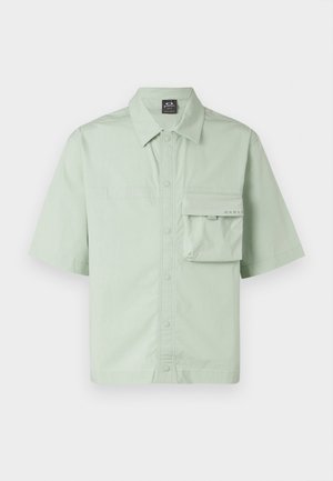 Short-sleeve shirt in light green fabric, featuring a button-up front, collar, and a single patch pocket with logo detailing.