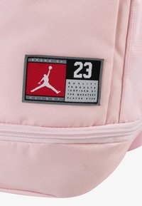 Rosa stoffsekk med en logopatch med rød bakgrunn, silhuettgrafikk og tekstbeskrivelse "Merket av Flight" og "23."