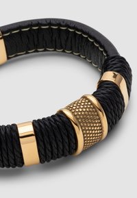 Black braided leather bracelet with gold-toned metal accents, including textured and smooth sections, featuring stitching detail along the edges.