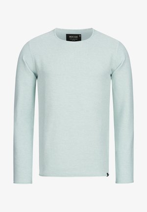 Vaaleansininen pitkähihainen neulepaita, jossa on pyöreä kaula-aukko, teksturoidusta kankaasta ja pieni musta logotagi haalaria lähellä.