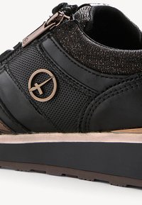 Black sneaker featuring a textured upper with a metallic zip closure and logo accent. The sole is supportive with a slightly elevated design.