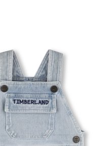 Salopette in denim azzurro chiaro con spalline, tasca frontale con ricamo "TIMBERLAND" e bottoni in metallo scuro.