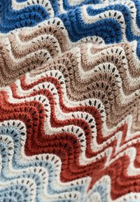 Tissu au crochet multicolore avec des motifs ondulés en zigzag bleu, marron, rouge et blanc, créant un effet de texture en couches.